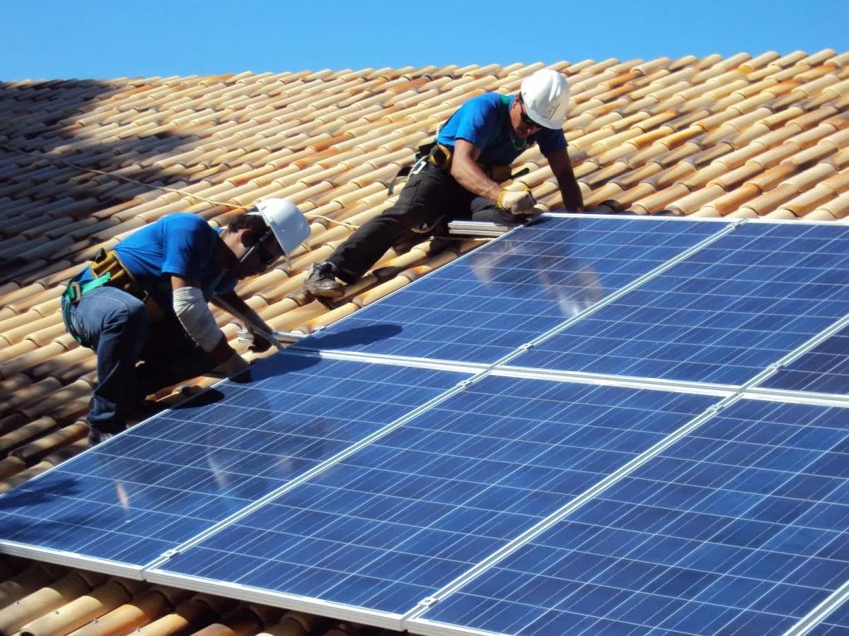 Dois profissionais instalando placas solares no telhado de uma casa